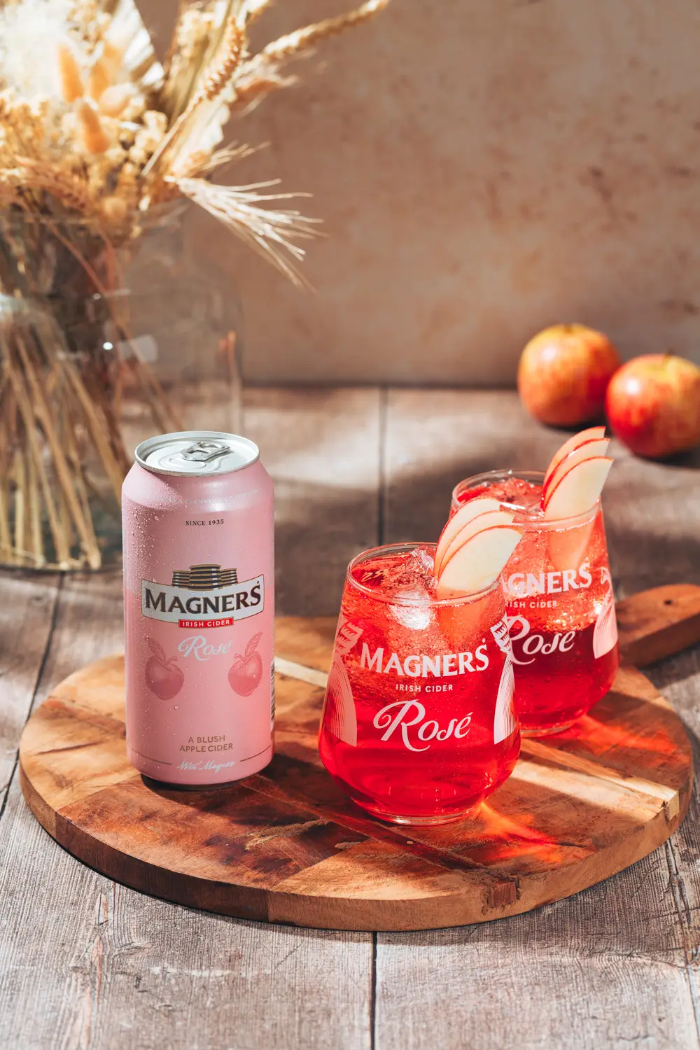 Magners Rose cider can on a wooden table with two glasses